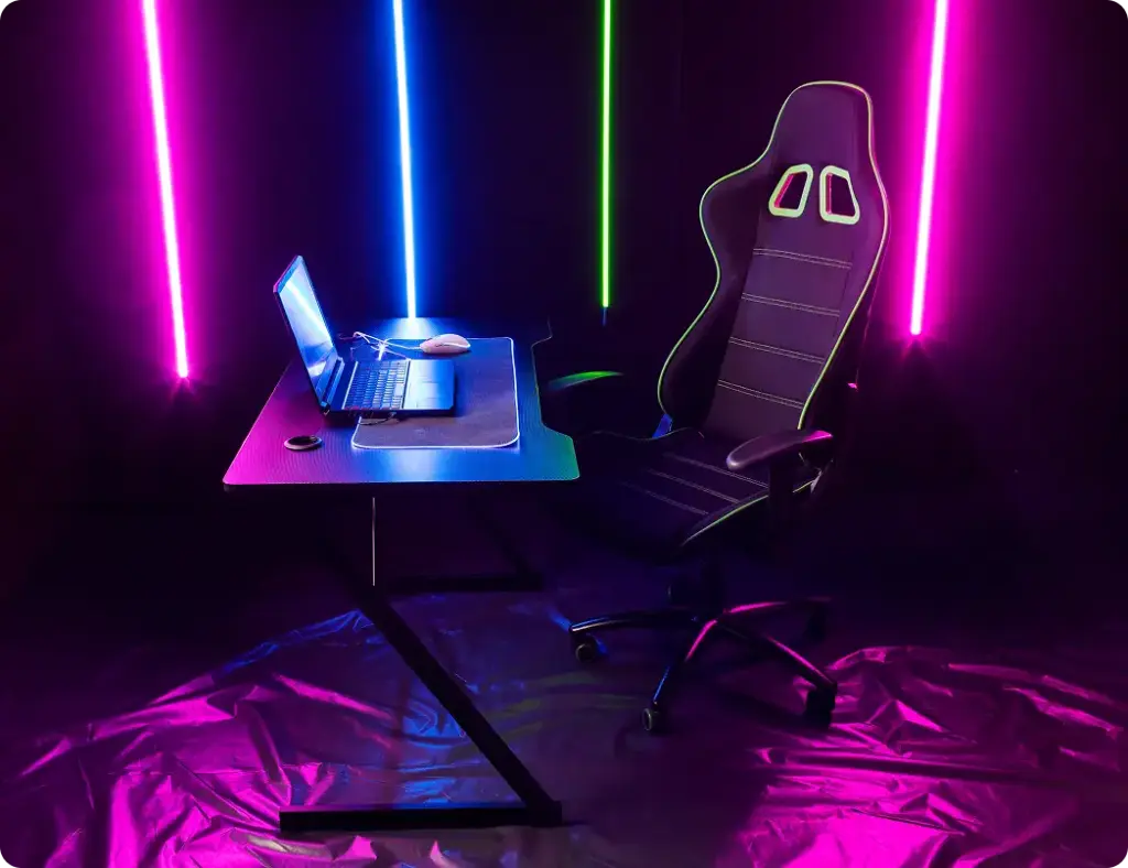 Een strakke gamingopstelling met een laptop op een modern bureau, een ergonomische gamingstoel en levendige neonverlichting in roze, blauw en groen, wat een futuristische sfeer creëert