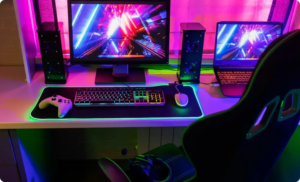 Een levendige gamingopstelling met twee monitoren waarop kleurrijke, futuristische beelden te zien zijn. Op het bureau staan een verlicht toetsenbord, een muis, luidsprekers en een gamingstoel, allemaal verlicht door neonlampen